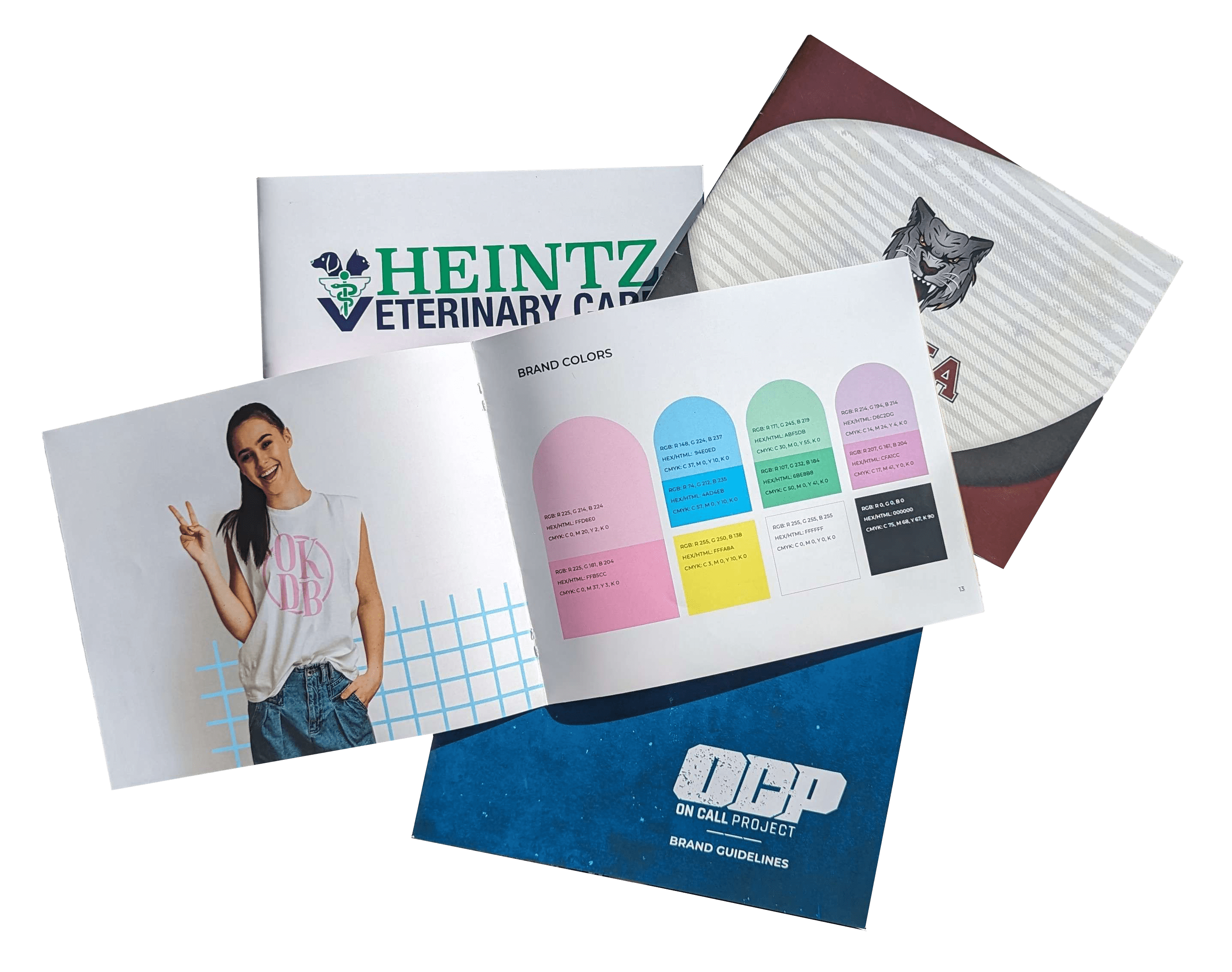 Flat view of a bunch of printed brand books together. Pictured is the covers of Heintz Veterinary Care, Atoka Public Schools, and On Call Project, with the Okie Dokie Bakery book on top, open to a page describing their colors.